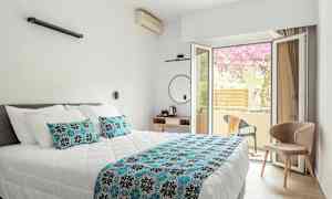 Et hotelværelse med en dobbeltseng og et åbent glasvindue ud til en altan. (AI-genereret tekst)