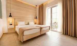 To enkeltsenge i et lyst rum med store glasdøre og beige gardiner. (AI-genereret tekst)