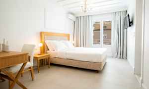 Et lyst hotelværelse med en behagelig dobbeltseng, et skrivebord og en stol. (AI-genereret tekst)