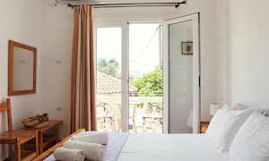 Et lyst soveværelse med hvide vægge, en seng med hvidt sengetøj og en balkon udenfor glasdøre. (AI-genereret tekst)