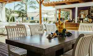 Et bord med hvide stole og en glasbeholder med citroner står udendørs nær en træbygning. (AI-genereret tekst)