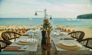 Et dækket bord på en restaurant ved stranden med havet i baggrunden. (AI-genereret tekst)