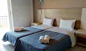 Rummet har to enkeltsenge med blåt sengetæpper og hvide puder samt rullede håndklæder placeret på sengen. (AI-genereret tekst)