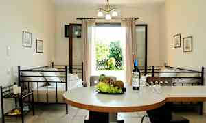 Et indendørsmiljø med et bord med frugt og en vinflaske, to senge og en åben dør, der fører ud til en have. (AI-genereret tekst)