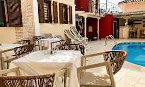 Borde og stole ved en udendørs pool, omgivet af bygninger med skodder. (AI-genereret tekst)