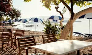 Udendørsmøbler med stole og borde tæt på en strand med parasoller. (AI-genereret tekst)