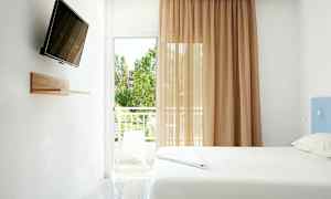 Et lyst værelse med en seng, en vægmonteret TV og en balkon med udsigt. (AI-genereret tekst)