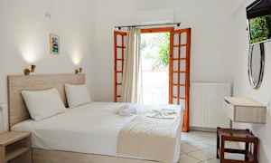 Et hotelværelse med en dobbeltseng og åben altandør. (AI-genereret tekst)