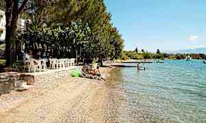 En strand med liggestole, badebro og klart blåt vand. (AI-genereret tekst)