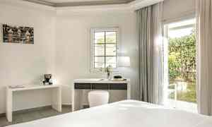 Et lyst hotelværelse med et skrivebord og en vinduesdør ud til en have. (AI-genereret tekst)