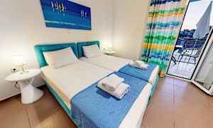 Et hotelværelse med to enkeltsenge, blåt sengetæppe og et maleri ovenover. (AI-genereret tekst)