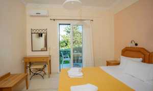 Et hotelværelse med en redt seng, et skrivebord og en stol samt en glasdør, der fører til en balkon. (AI-genereret tekst)