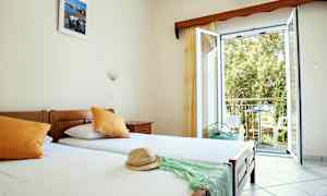 Et hotelværelse med enkeltsenge, åbent vindue og udsigt til balkon. (AI-genereret tekst)