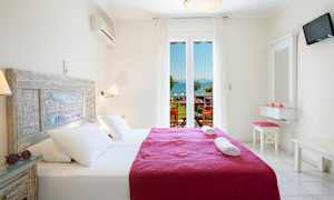 Et lyst og luftigt hotelværelse med en dobbeltseng udstyret med hvide lagner og et lilla tæppe. Vindue med udsigt over havet og en balkon. (AI-genereret tekst)