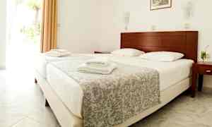 Billede af et hotelværelse med en dobbeltseng, foldede hvide håndklæder og et glas med drikke på natbordet. (AI-genereret tekst)