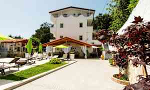 Udendørs miljø med en treetagers bygning, liggestole og grønne parasoller. (AI-genereret tekst)