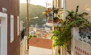 En gyde med altaner og bevoksning, udsigt over hustage og skovklædt bjerg. (AI-genereret tekst)