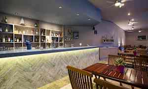 Bar med træborde og hylder fyldt med flasker. (AI-genereret tekst)