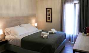 Hotelværelse med en dobbeltseng, natborde med lamper, sammenrullede håndklæder på sengen og et vindue med gardiner. (AI-genereret tekst)