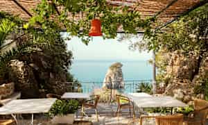 Omgivelser med udsigt til havet, borde og stole på en veranda med grønne planter. (AI-genereret tekst)