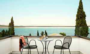 To stole og et bord på en terrasse med udsigt over havet. (AI-genereret tekst)