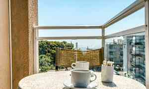 En balkon med udsigt over havet. På bordet er der to kaffekopper og en beholder med sukkerposer. (AI-genereret tekst)