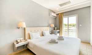 Moderne møbleret hotelværelse med dobbeltseng og hvide lagner. Vindue med lysindfald. (AI-genereret tekst)