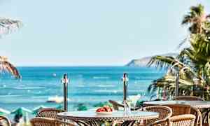 Udsigt over bord med drikkevarer og frugt mod havet. (AI-genereret tekst)