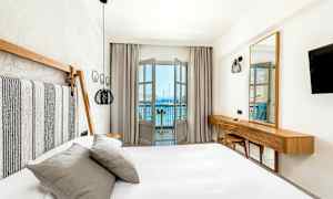 Et lyst og moderne indrettet hotelværelse med seng og udsigt over havet fra en altan. (AI-genereret tekst)