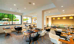 En moderne restaurant med træmøbler, vinduer med udsigt til en udendørsservering og flere borddækninger. (AI-genereret tekst)