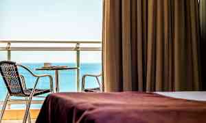 Værelse med brun gardin, udsigt over havet og møbleret altan. (AI-genereret tekst)