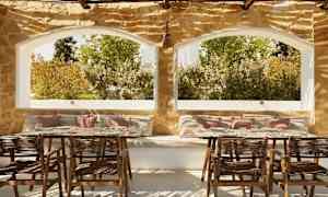 En terrasse med siddepladser og borde, stenmur og store vinduer med udsigt til grønne områder. (AI-genereret tekst)