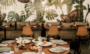 Et dækket træbord omgivet af stole, med en baggrund af vægmalerier med plantemotiver. (AI-genereret tekst)