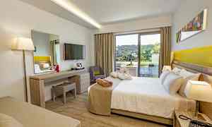 Et hotelværelse med seng, skrivebord, TV og en balkon med udsigt til grønne omgivelser. (AI-genereret tekst)