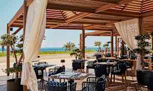 Udendørsområde med træmøbler, hvide gardiner og havudsigt. (AI-genereret tekst)