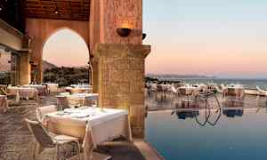 Udendørs spiseområde med dækkede borde ved siden af en pool og havudsigt ved solnedgang. (AI-genereret tekst)