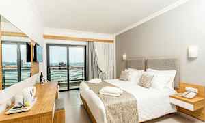 Et hotelværelse med en stor seng, lyse møbler og en balkon med udsigt. (AI-genereret tekst)