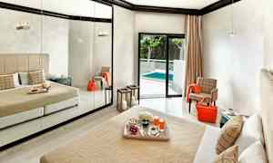 Et hotelværelse med en stor spejlvæg, en seng med beige sengetæppe og puder samt en altandør, der fører ud til en pool. (AI-genereret tekst)