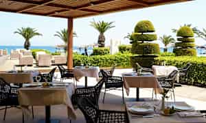 Udendørs servering med dækkede borde, palmer og udsigt til havet. (AI-genereret tekst)