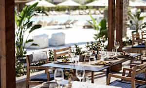 Udendørsmøbler med mad og drikke serveret, poolområde i baggrunden. (AI-genereret tekst)