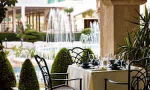 Et udendørs spiseområde med udsigt til en have med springvand. (AI-genereret tekst)