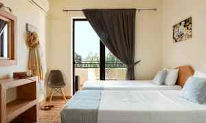 Et værelse med to enkeltsenge, et stort vindue med mørke gardiner og altanmøbler udenfor. (AI-genereret tekst)