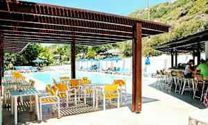 Udendørs poolområde med solsenge, parasoller, borde og stole under skyggefulde tage. (AI-genereret tekst)