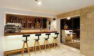 En moderne bardisk med høje stole, flasker på hylder og lys belysning. (AI-genereret tekst)