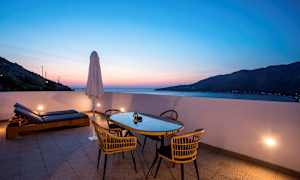 Terrasse med bord, stole og liggestole ved solnedgang. (AI-genereret tekst)