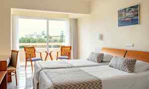 Et hotelværelse med to enkeltsenge, en siddegruppe og udsigt til grønne omgivelser. (AI-genereret tekst)