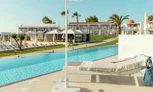 En solseng med et tæppe ved kanten af en pool, med en parasol i forgrunden og hotelbygninger i baggrunden. (AI-genereret tekst)