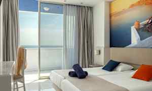 Hotelværelse med dobbeltseng, farverige puder og balkon med havudsigt. (AI-genereret tekst)