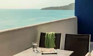 To stole med et grønt tæppe på den ene, stående ved et bord med et glas vand og en avis, med havudsigt. (AI-genereret tekst)