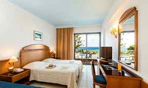 Et hotelværelse med to senge, et skrivebord, et spejl og en balkon med udsigt over havet. (AI-genereret tekst)